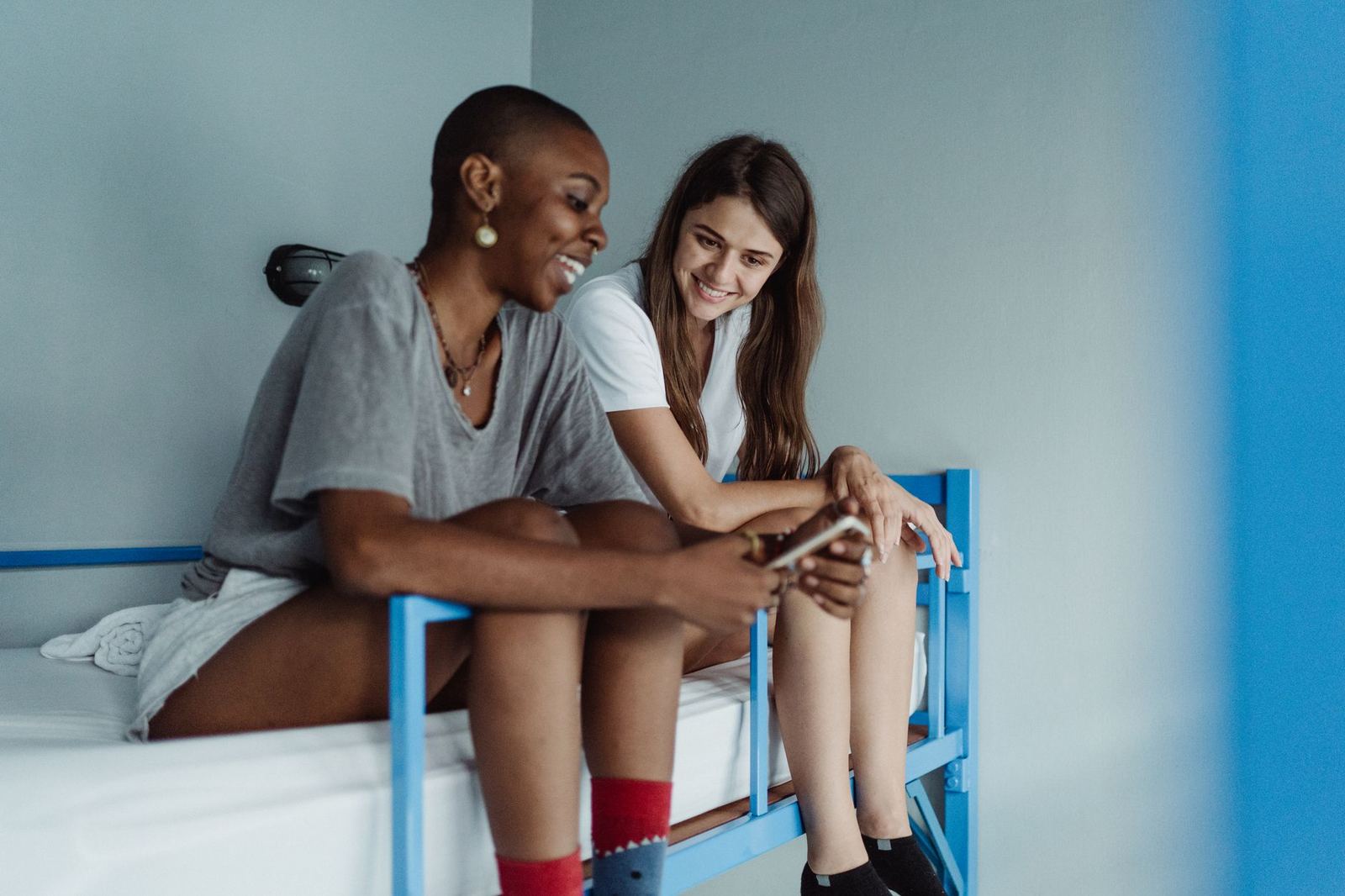 Two women relax and chat on a bunk bed in a modern hostel room, sharing a moment of connection.